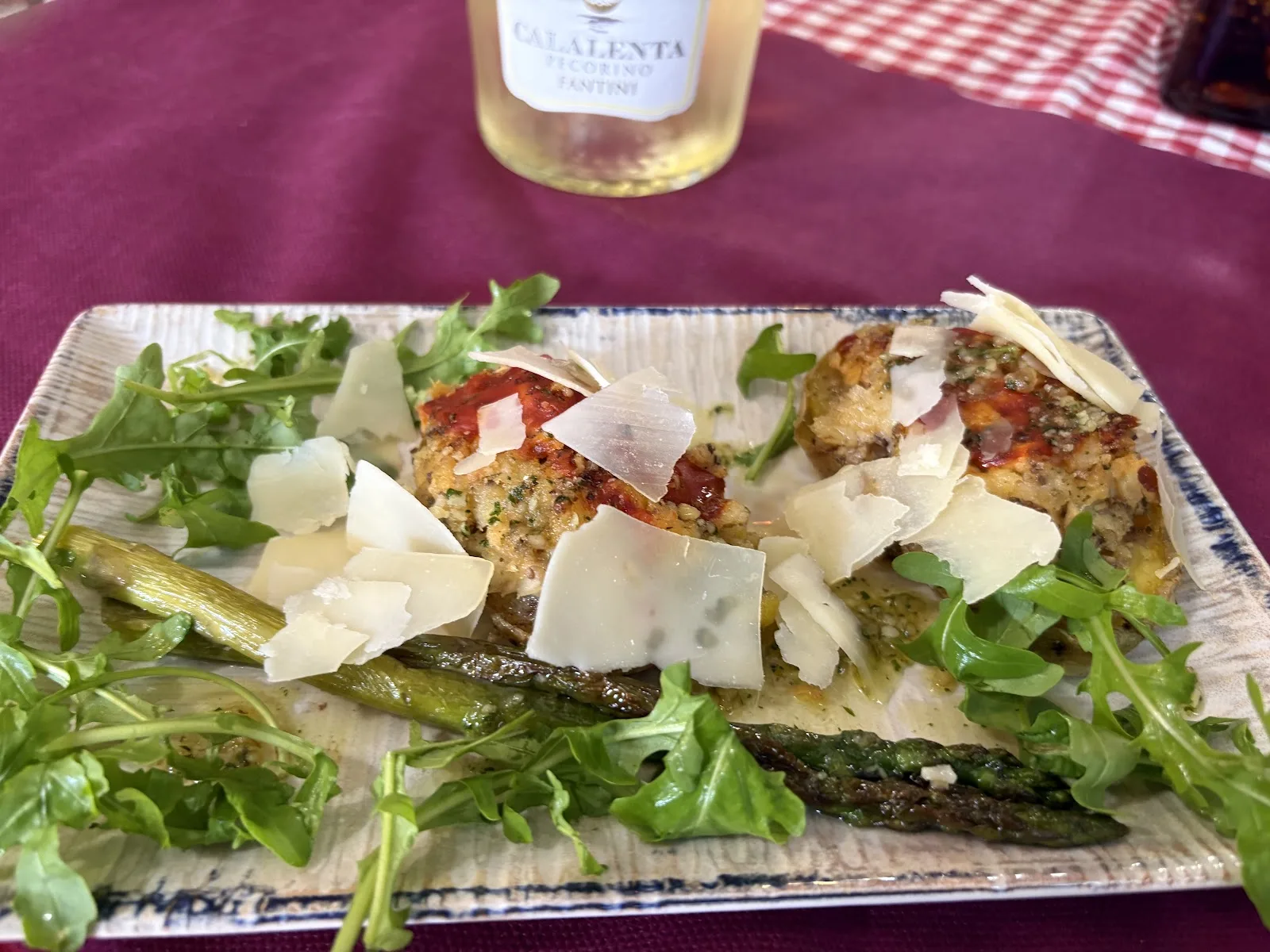 Antipasto gratinado con lascas de parmesano, rúcula y espárragos verdes a la plancha, servido en plato alargado