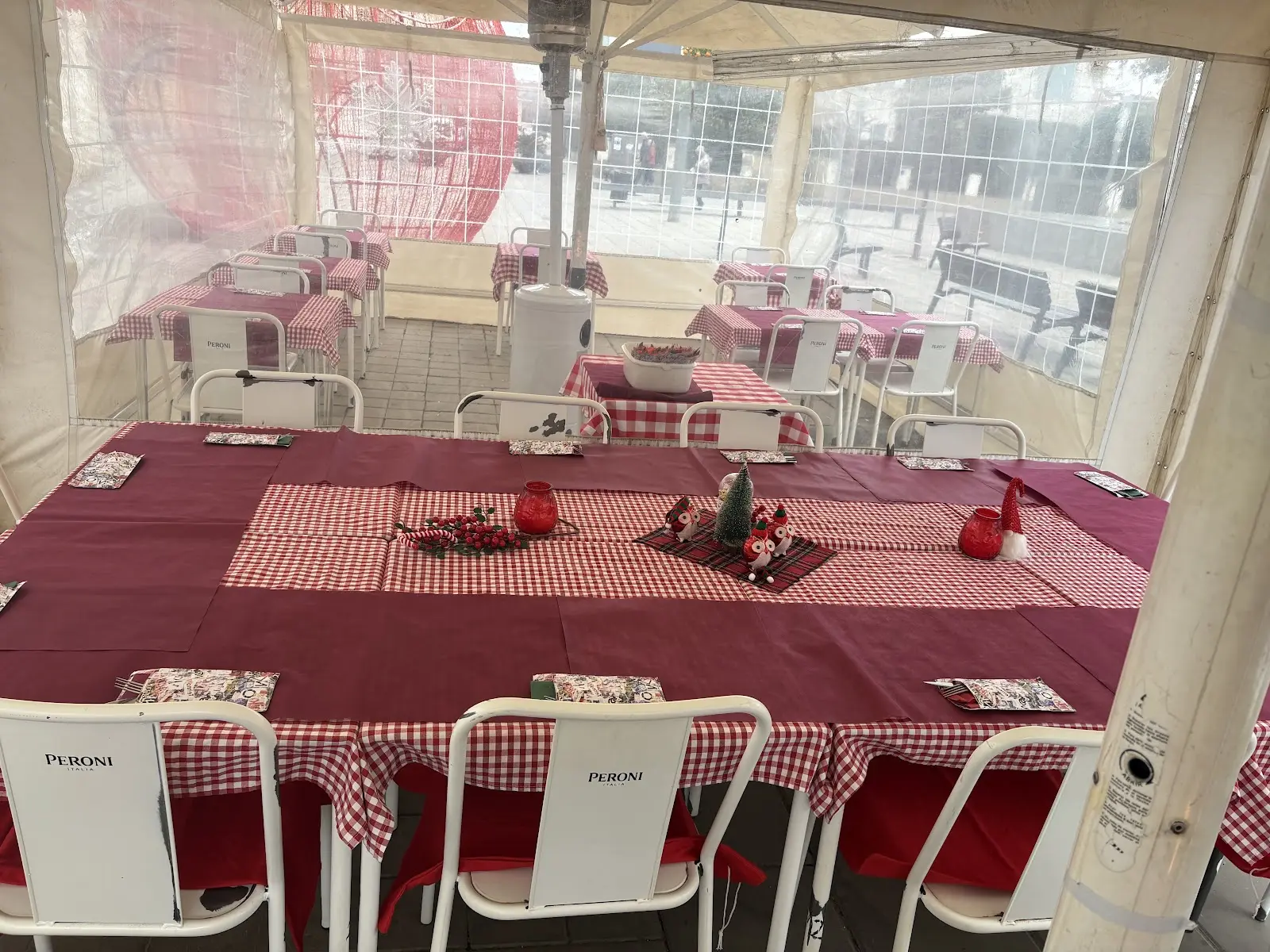 Interior de la carpa cerrada de la terraza, con una mesa larga preparada para un grupo, mantel burdeos con camino de mesa de cuadros y sillas blancas