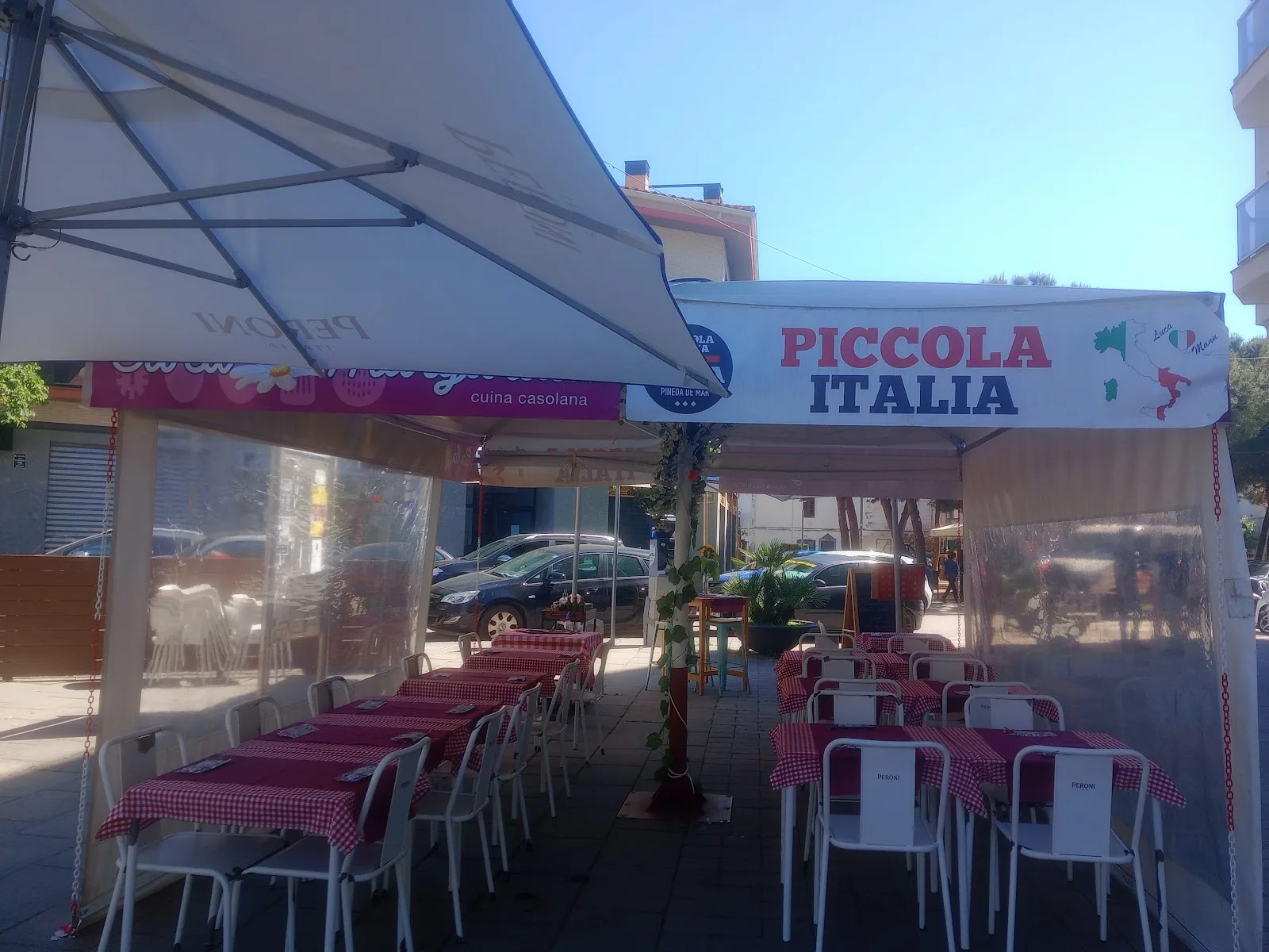 Terraza de Piccola Italia bajo el toldo blanco, con mesas vestidas y la plaza de Pineda de Mar alrededor